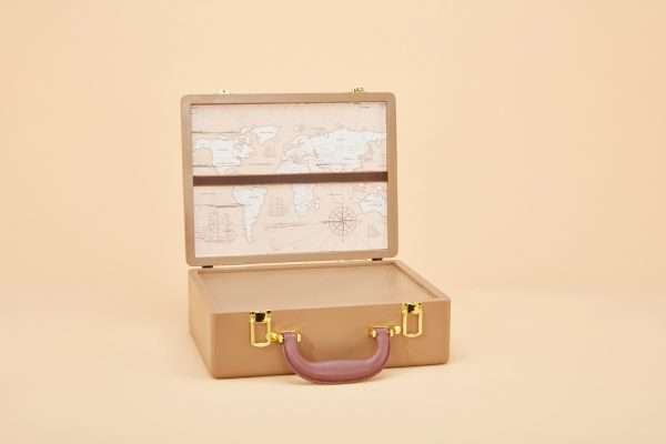 An urn that looks like a tan leather suitcase with gold latches and a brown handle. It is it is open and is lined with a map of the world