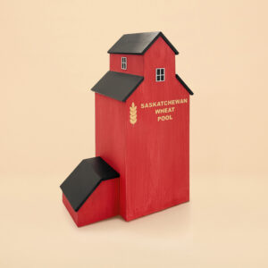 An urn that looks like a red grain elevator. The words "Saskatchewan Wheat Pool" are painted on the wooden structure. It has a grassy base