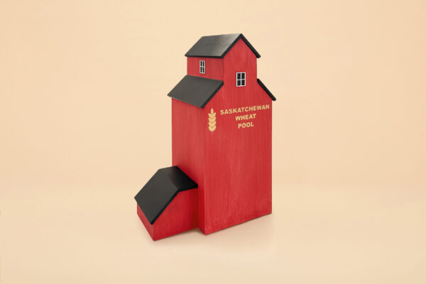 An urn that looks like a red grain elevator. The words "Saskatchewan Wheat Pool" are painted on the wooden structure. It has a grassy base