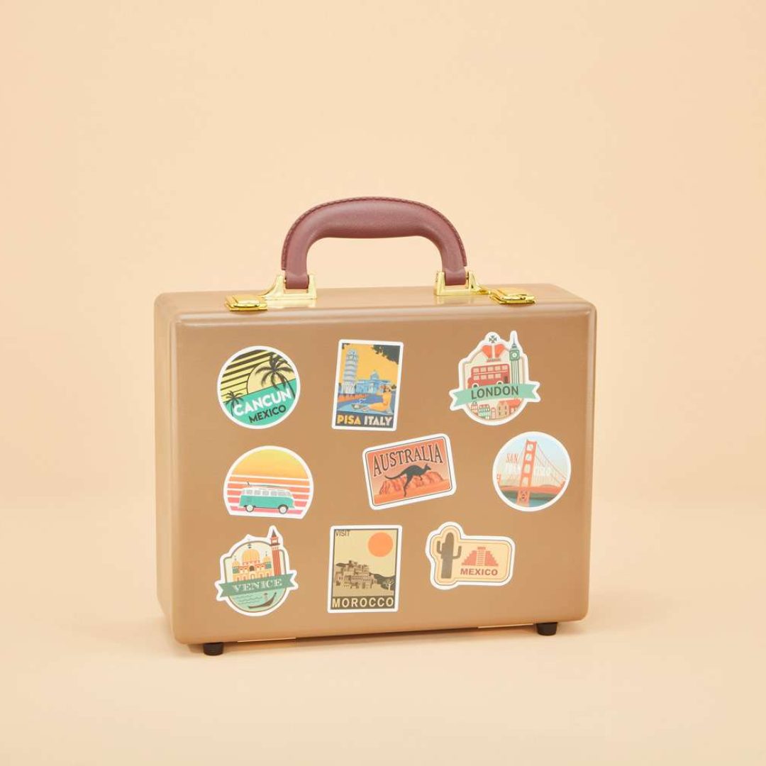 An urn that looks like a tan leather suitcase with gold latches and a brown handle. It is covered in stickers of cities around the world